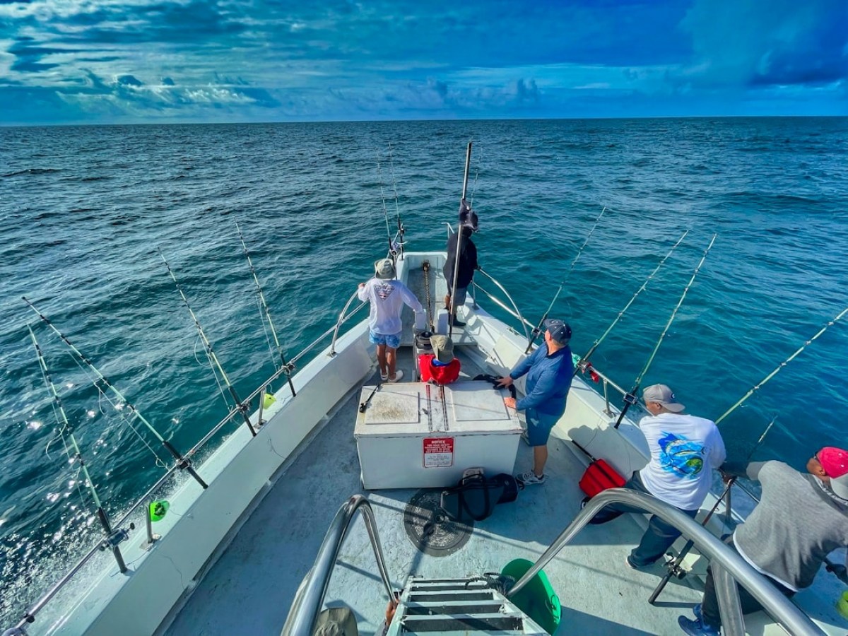 People on a boat fishing in the ocean under a cloudy sky.