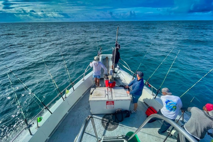 People on a boat fishing in the ocean under a cloudy sky.