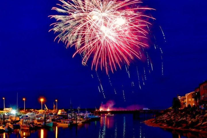 Bright fireworks in night sky over a harbor with boats and buildings.