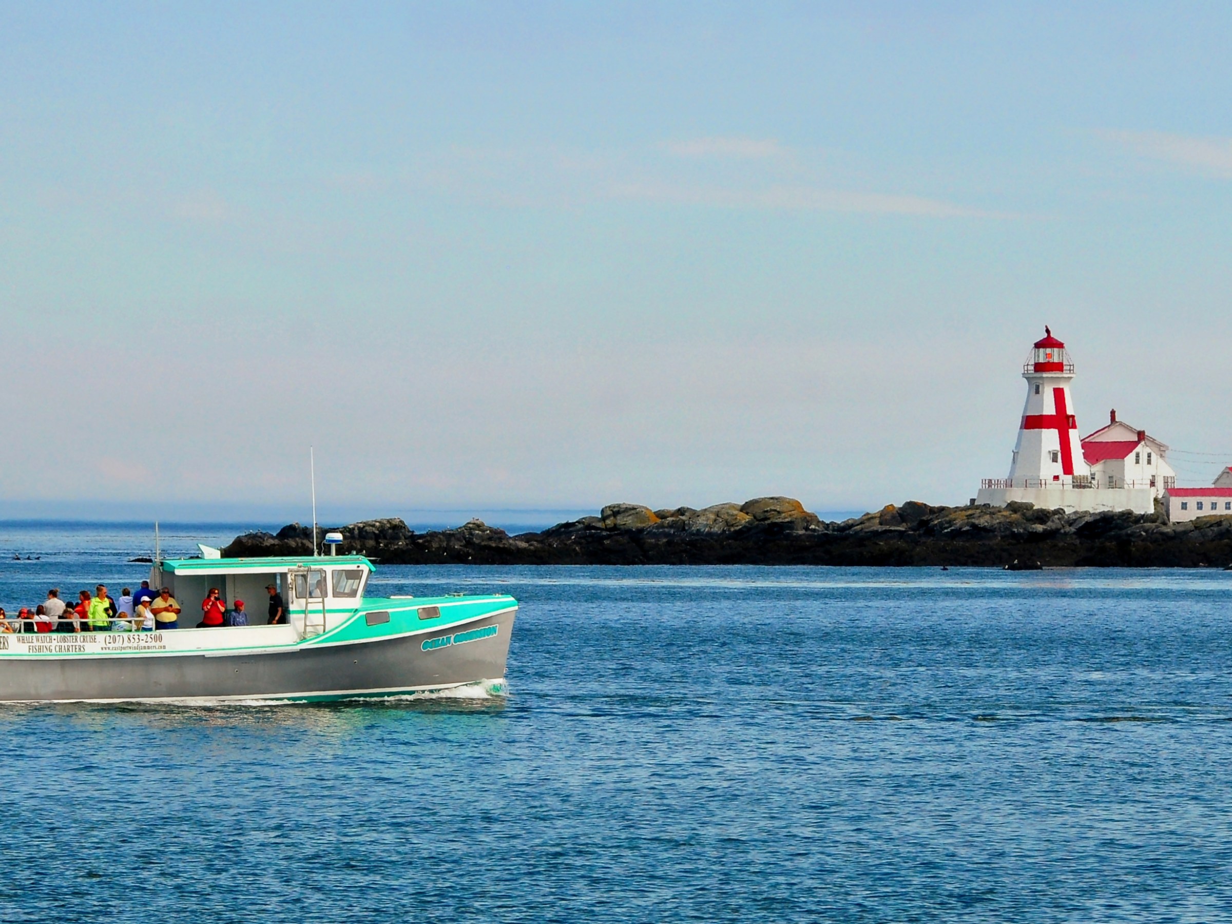 Boat with people on water, lighthouse on small island in background.