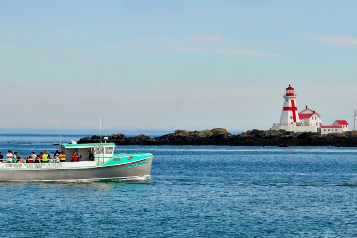 Boat with passengers near a lighthouse on a small island.