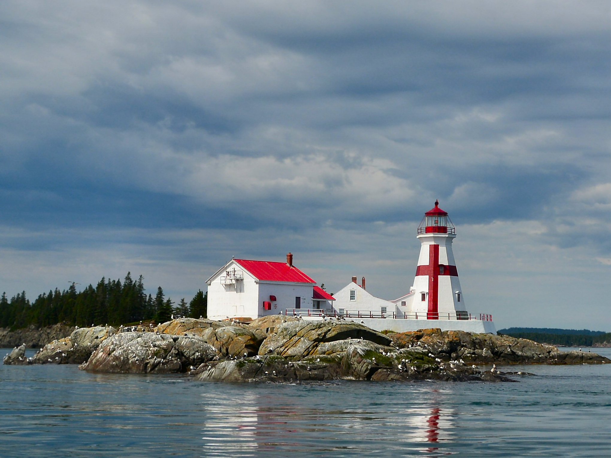 Lighthouse with red roof on rocky island with cloudy sky.