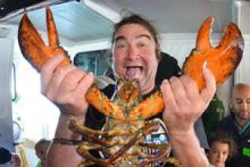 Person excitedly holds large lobster with raised claws on a boat.