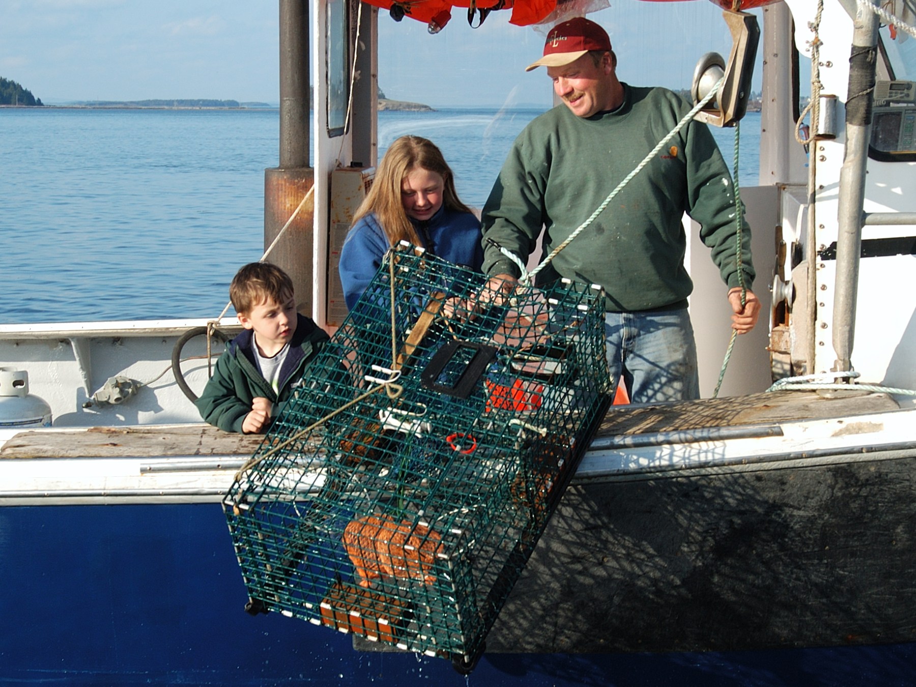 Two adults and a child haul a lobster trap on a boat.